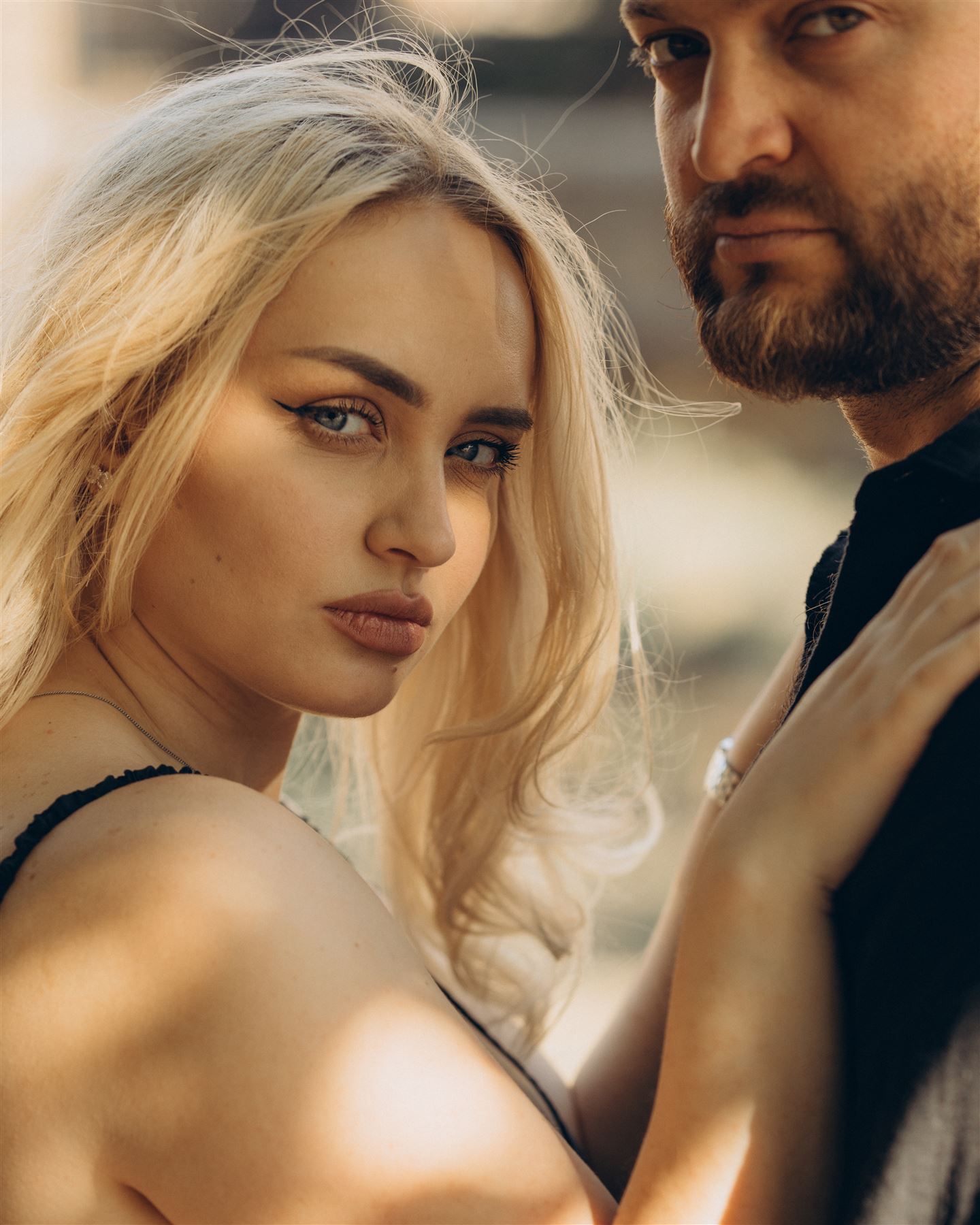 She looks into the camera, he stands behind her